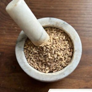 Ashwagandha root cut and sifted in a mortar and pestle with Withania somnifera plant background - The Herb Peddler