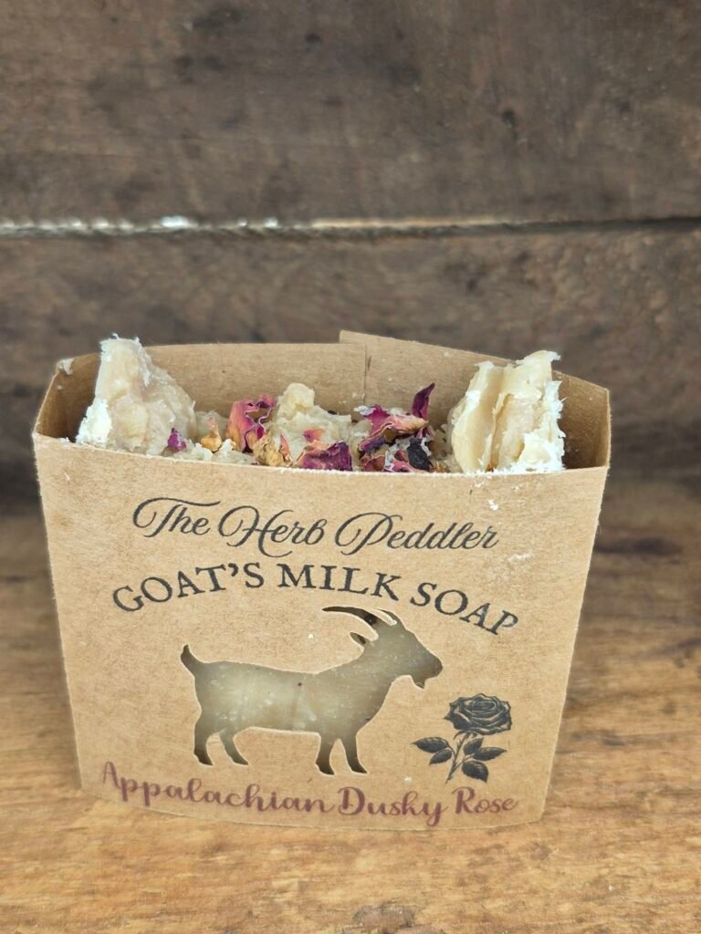Appalachian Dusky Rose goat milk soap bar with soft pink hues, displayed with dried roses and cedar sprigs against a dusky Appalachian sunset background - The Herb Peddler