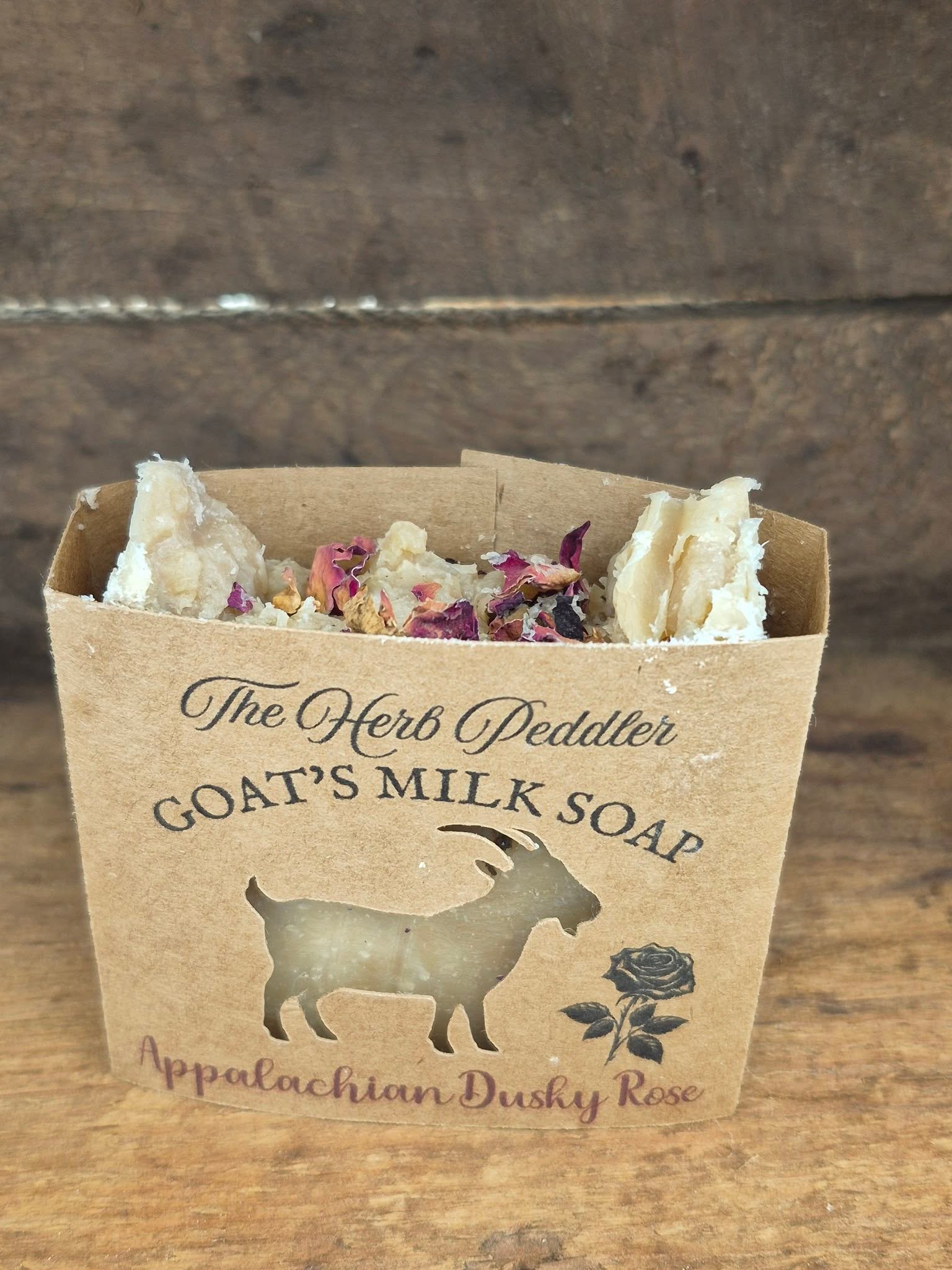 Appalachian Dusky Rose goat milk soap bar with soft pink hues, displayed with dried roses and cedar sprigs against a dusky Appalachian sunset background - The Herb Peddler